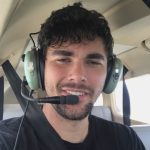 Smiling man wearing a green aviation headset with microphone in a small airplane cockpit.