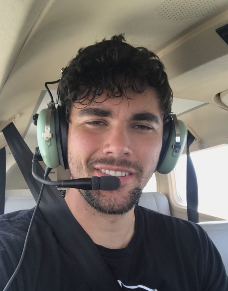 Smiling man wearing a green aviation headset with microphone in a small airplane cockpit.