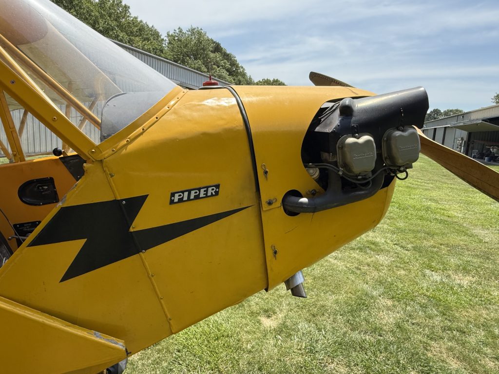 N6625H J3 Cub 1946 - Countrywide Flyers | Orlando Apopka X04 Close-up of a yellow Piper airplane’s nose with the engine exposed, sitting on a grassy airfield under a clear sky.