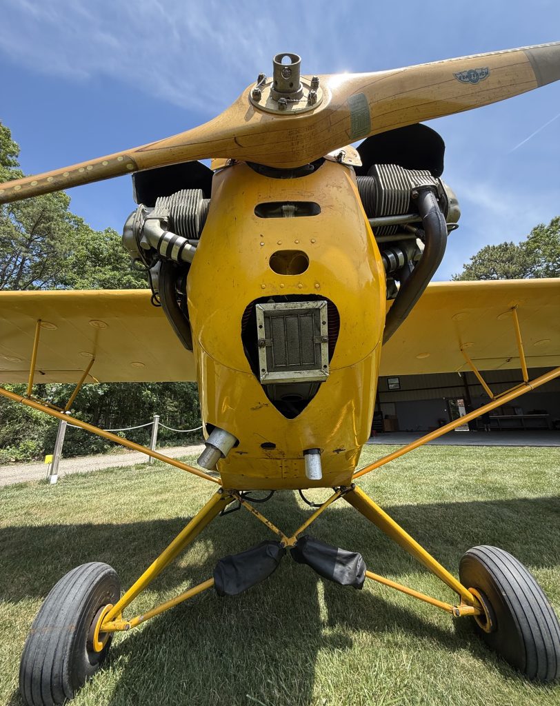 N6625H J3 Cub 1946 - Countrywide Flyers | Orlando Apopka X04 Front view of a yellow vintage airplane with a wooden propeller and exposed engine cylinders on a grassy airfield against a blue sky.