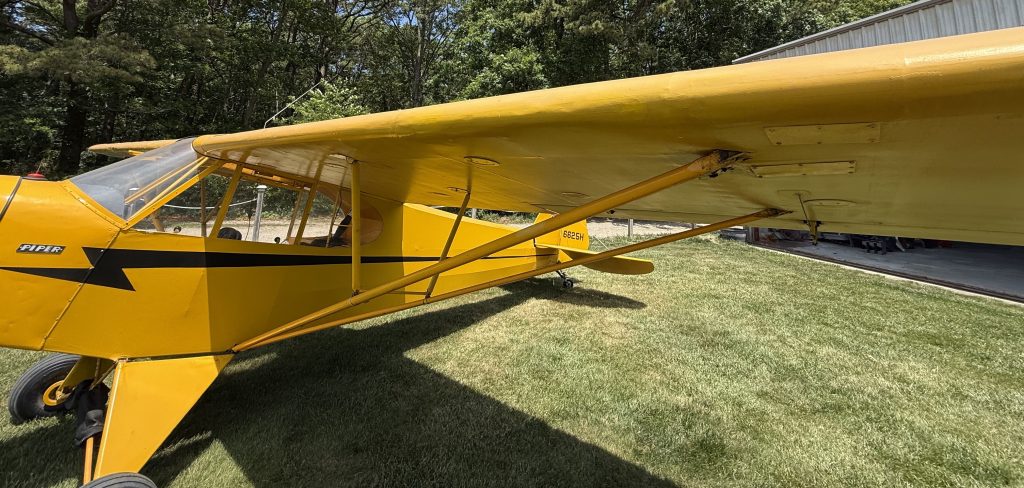 N6625H J3 Cub 1946 - Countrywide Flyers | Orlando Apopka X04 Yellow Piper Cub airplane parked on a grassy field beside a hangar, with a high wing and tailwheel visible.