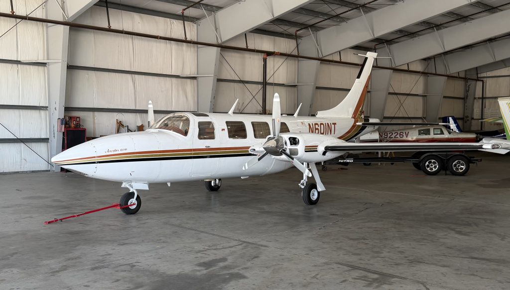 White private jet with gold/brown stripes inside a hangar, registration N60NT visible on fuselage.