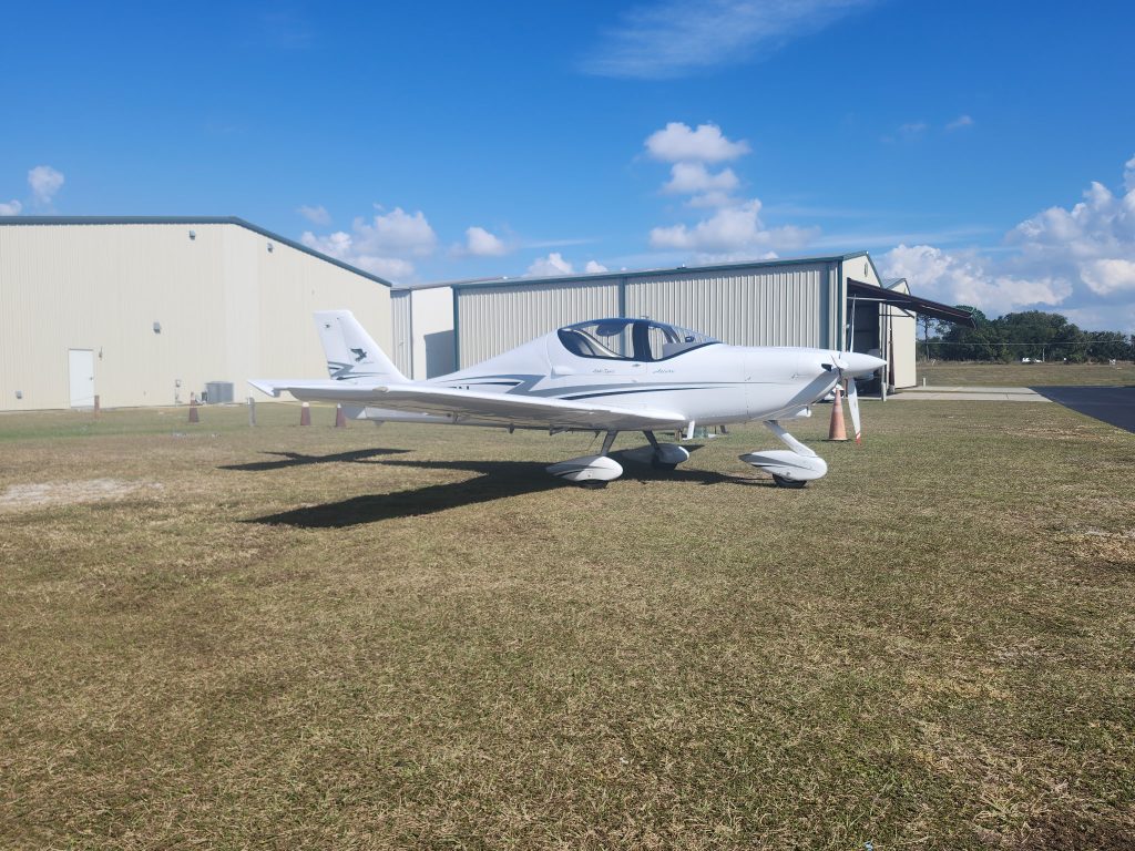 N207TN - Countrywide Flyers | Orlando Apopka X04 Small white single-engine airplane on grass near hangar under blue sky with scattered clouds, tail facing left.