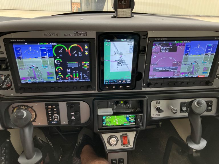 Cockpit of a small aircraft with three large digital screens showing flight instruments and navigation.