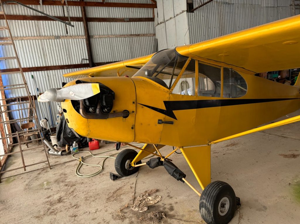 N42901 J3 C65 - Countrywide Flyers | Orlando Apopka X04 Yellow vintage single-engine airplane in a hangar with the engine exposed and propeller in front, landing gear visible.