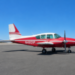 Red and white single-engine propeller airplane parked on a tarmac under a clear blue sky.