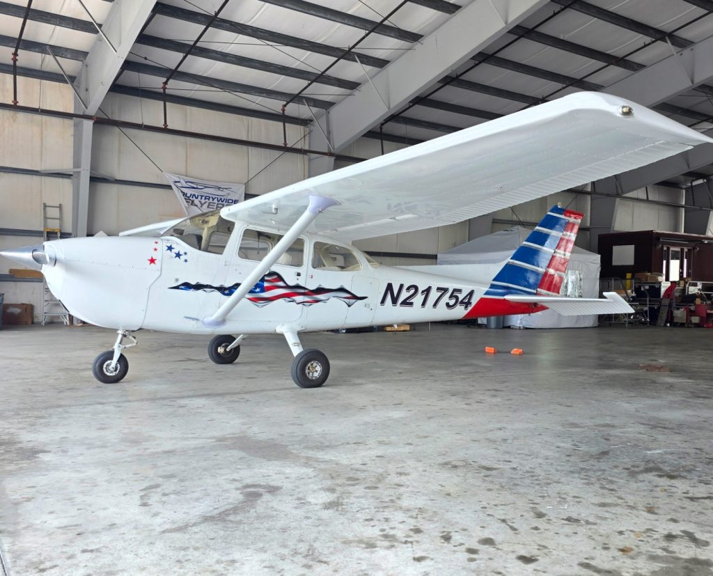 White single-engine high-wing aircraft with red, white, and blue patriotic livery and tail number N21754 inside a hangar.