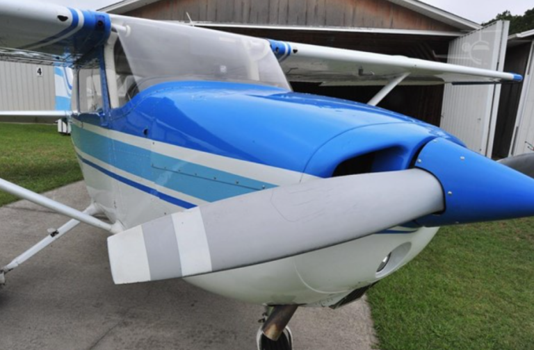 Blue and white single-engine airplane parked on a taxiway in front of a hangar.
