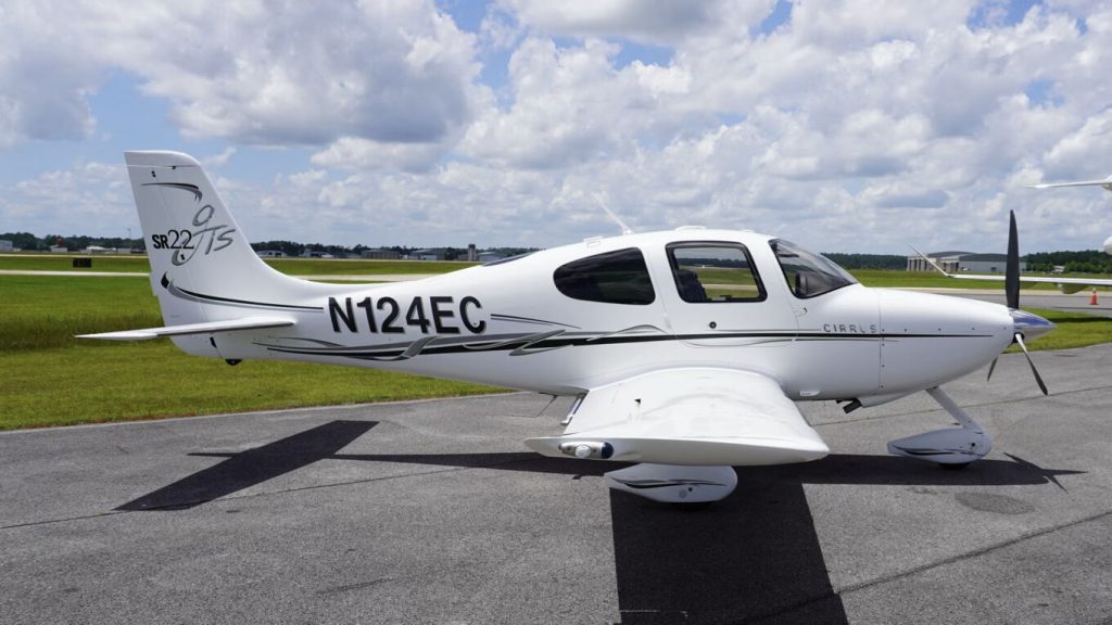 White Cirrus SR22 light aircraft with tail number N124EC parked on the taxiway against a blue sky.
