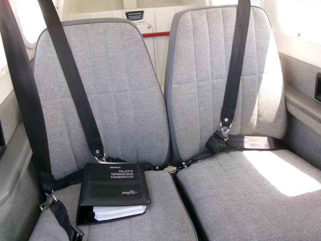 N4161Z Back Seats - Countrywide Flyers | Orlando Apopka X04 Two gray airplane seats with black seat belts; a Pilot's Operating Handbook rests on the center area between them.
