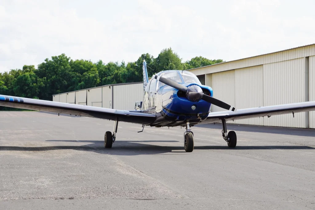 Blue single-engine airplane parked on the tarmac in front of a beige hangar on a clear day