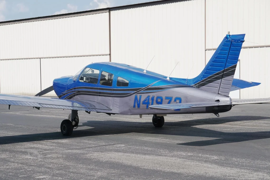 Blue single-engine propeller airplane parked on a tarmac beside a light-colored hangar, tail number N41972 visible on the fuselage.