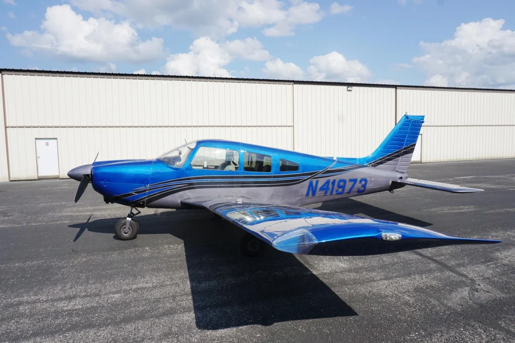 Blue single-engine airplane parked on a paved apron with a beige hangar in the background and tail number N41973.