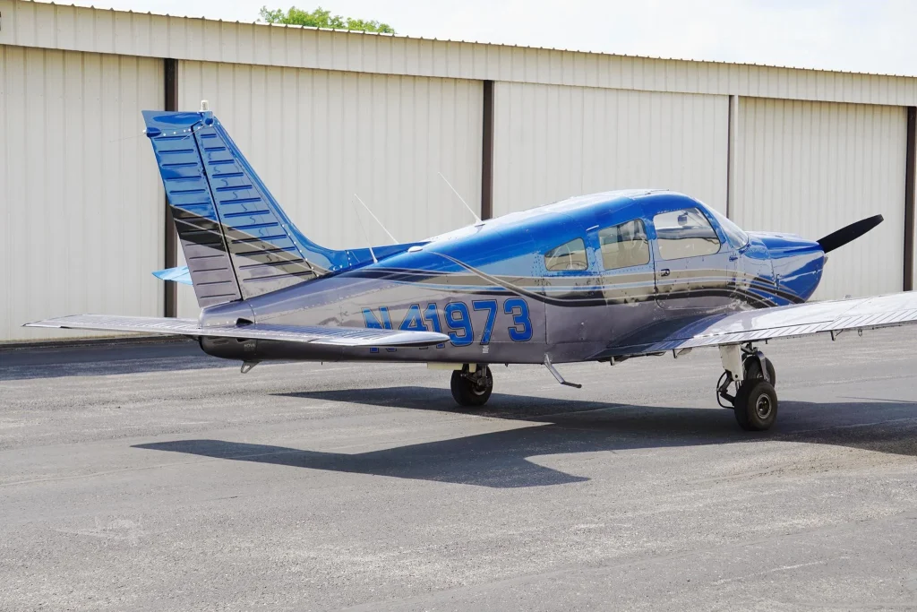 Blue single-engine propeller airplane parked on the tarmac in front of a beige hangar, registration N41973 visible on the fuselage.