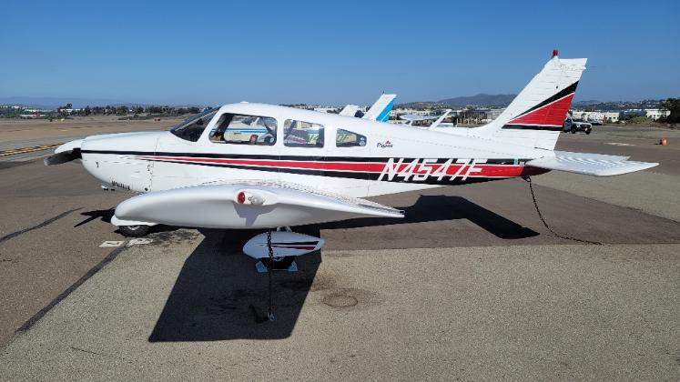 N4547F 12 - Countrywide Flyers | Orlando Apopka X04 Small white single-engine airplane with red and black stripes parked on an airport tarmac; a blue plane is visible in the background.
